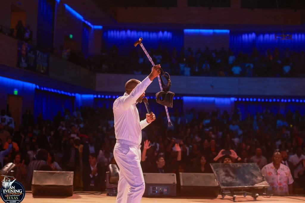 Prophet Isaiah Macwealth lifting a crutch before a packed hall at An Evening With Jesus, Texas