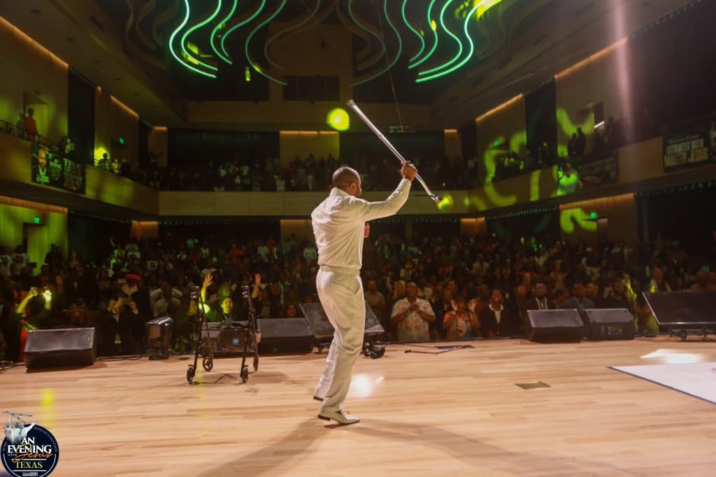 Prophet Isaiah Macwealth lifting a crutch before a cheering crowd at An Evening With Jesus, Texas