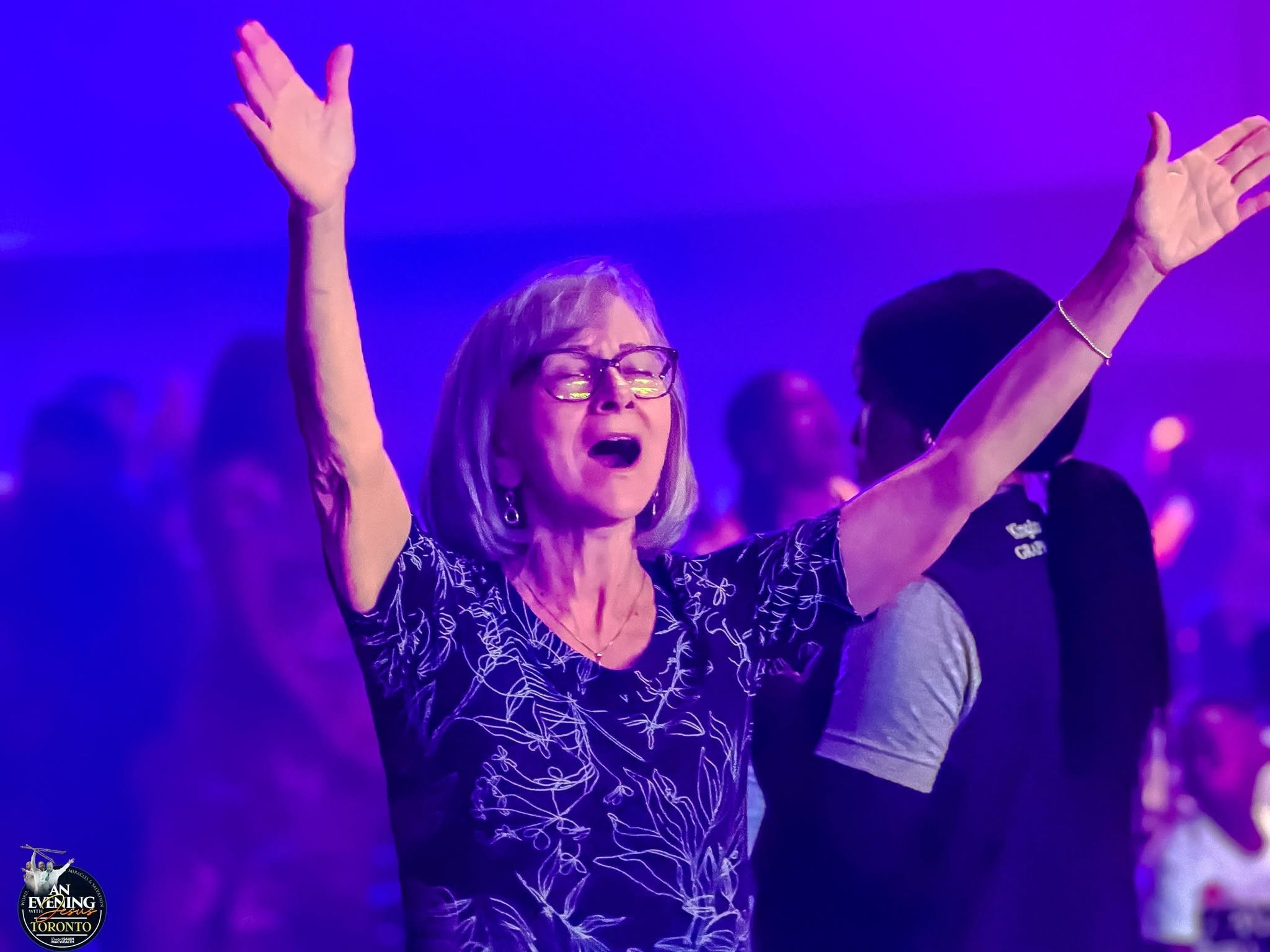 A worshipper with arms raised in praise at An Evening With Jesus, Toronto